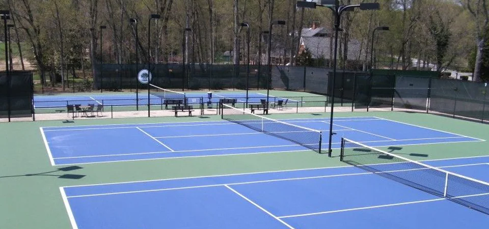 Outdoor pickleball courts with blue playing areas, green surrounds and nets